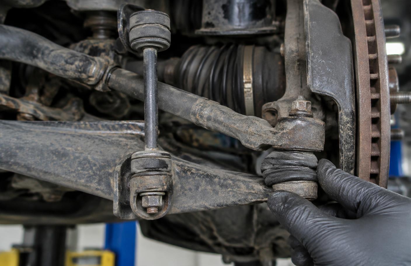 Zużyty łącznik stabilizatora i końcówka drążka sprawdzane dłonią mechanika
