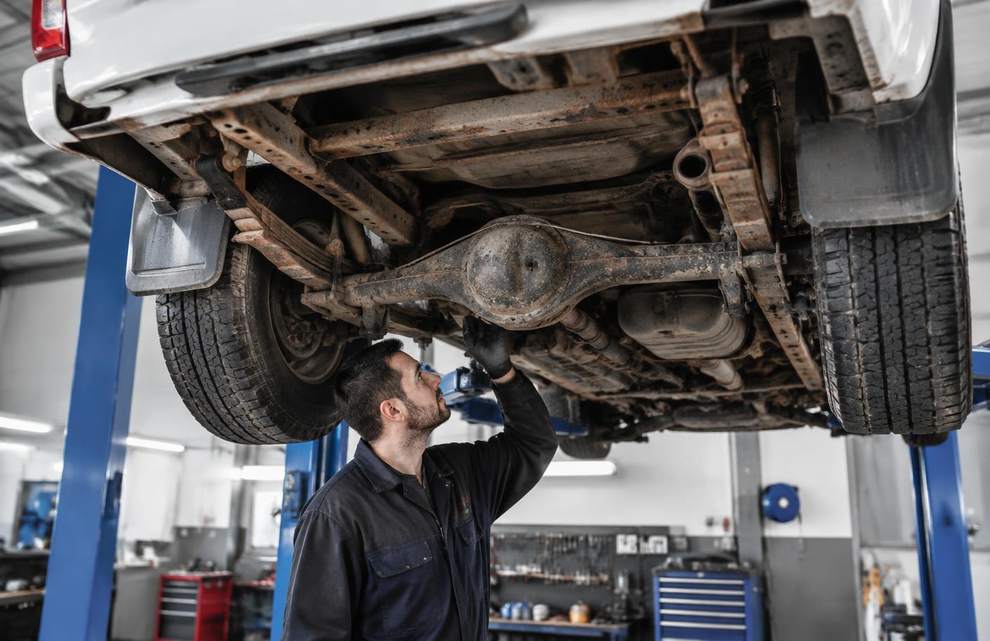 Mechanik sprawdzający skorodowany tylny most i ramę Mitsubishi L200 na podnośniku